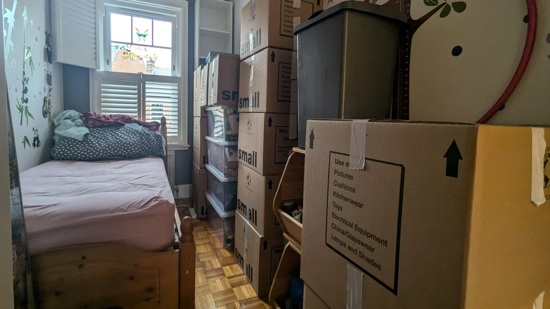 Wall of labelled cardboard boxes and reusable plastic crates stacked neatly in a West London house, packed by RAD Removals